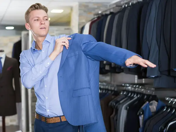 Gutt i klesbutikk tar på seg blå dressjakke. Foto til artikkel om kjøp av konfirmasjonsdress.