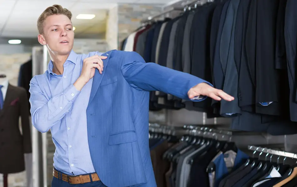 Gutt i klesbutikk tar på seg blå dressjakke. Foto til artikkel om kjøp av konfirmasjonsdress.
