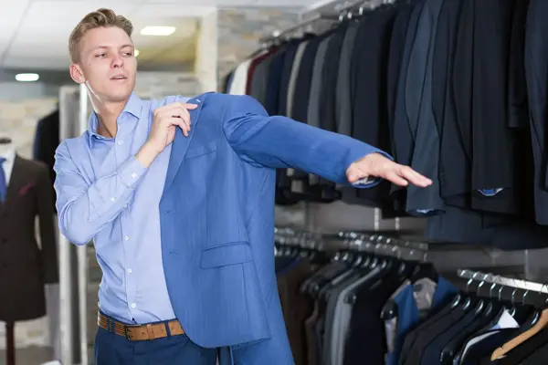 Gutt i klesbutikk tar på seg blå dressjakke. Foto til artikkel om kjøp av konfirmasjonsdress.
