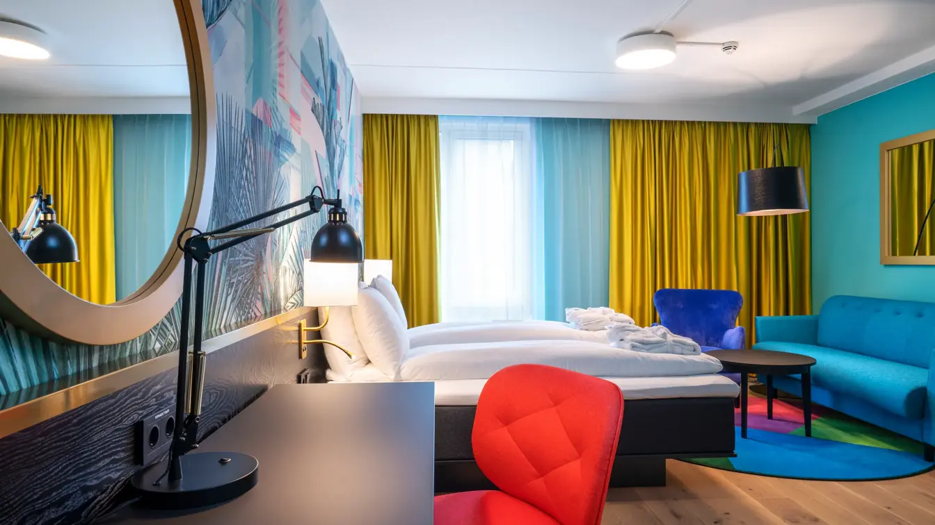 Skrivebord, rød stol, speil, dobbeltseng og sittegruppe i superior HCP rom på Thon Hotel Storo