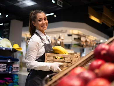 Working in grocery store. Supermarket worker supplying fruit department with food. Female worker holding crate with fruits.
