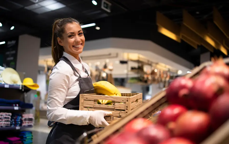 Working in grocery store. Supermarket worker supplying fruit department with food. Female worker holding crate with fruits.