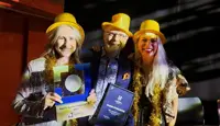 Tre ansatte på Oasen Storsenter har på seg gule hatter og holder diplom fra prisutdeling på kjøpesenterkonferanse.