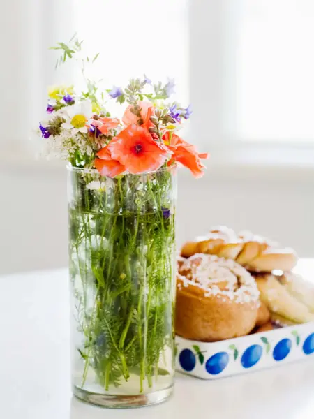Markblomster i vase og fat med kanelboller på bord 
