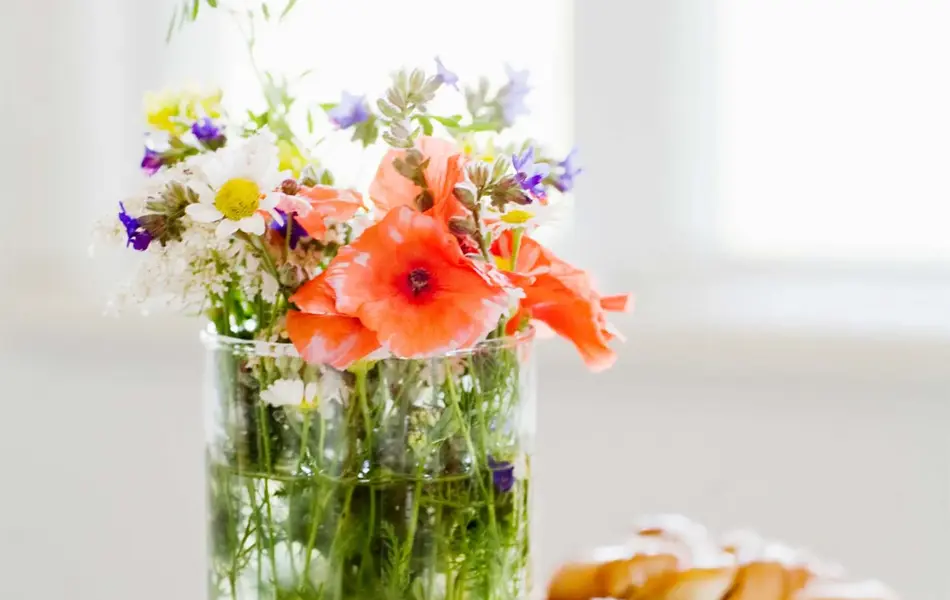 Markblomster i vase og fat med kanelboller på bord 