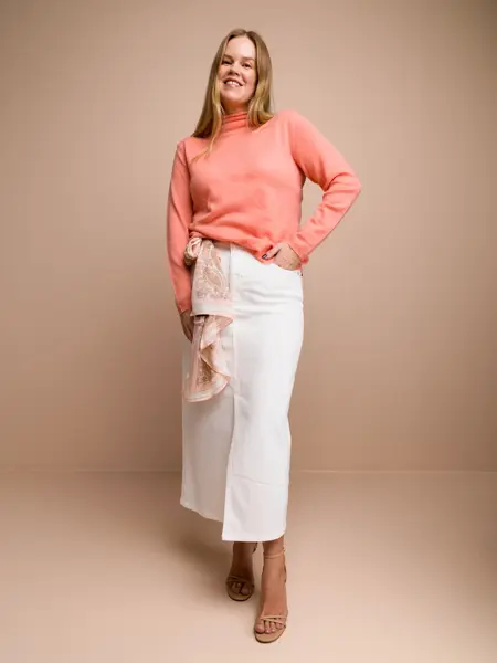 Damemodell med ferskenfarget høyhalset genser og hvitt olaskjørt