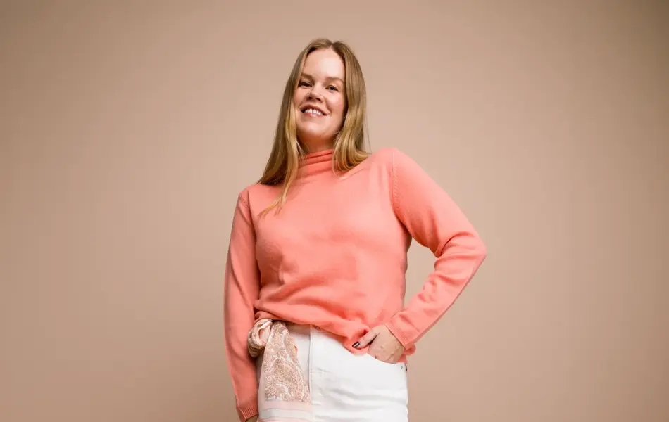 Damemodell med ferskenfarget høyhalset genser og hvitt olaskjørt