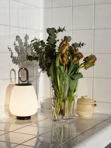 Flislagt kjøkkenkrok med bordlampe og vase med blomster.