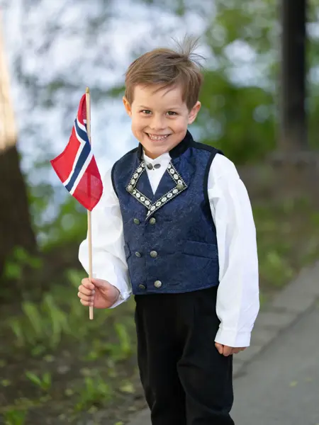 Gutt i mørk blå festdrakt, hvit skjorte og holder et flagg.