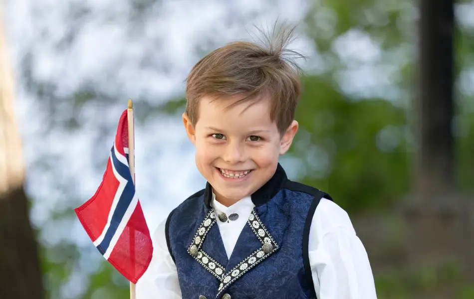 Gutt i mørk blå festdrakt, hvit skjorte og holder et flagg.