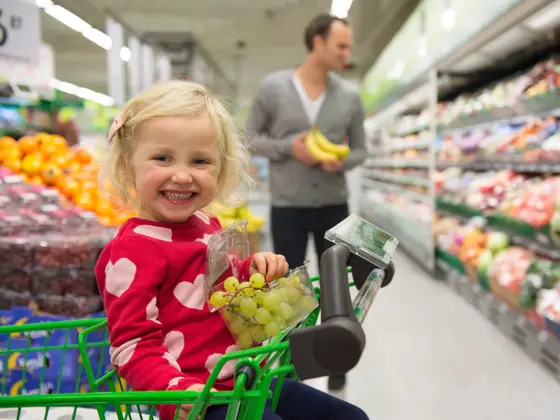 Jente sitter i handlekurv og spiser grønne druer