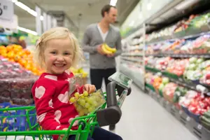Jente sitter i handlekurv og spiser grønne druer
