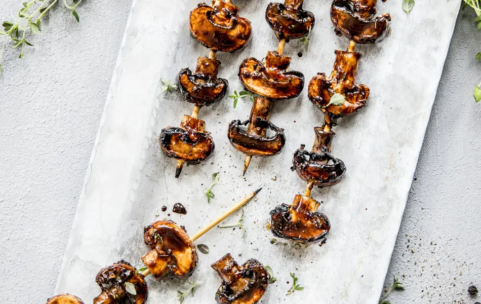 Grillspyd med grillet sopp på hvitt fat med urter rundt