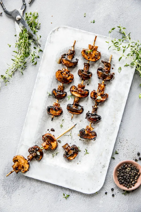 Grillspyd med grillet sopp på hvitt fat med urter rundt