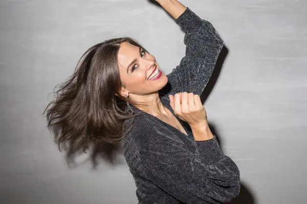 Jente i svart glitterkjole danser og smiler mot kamera