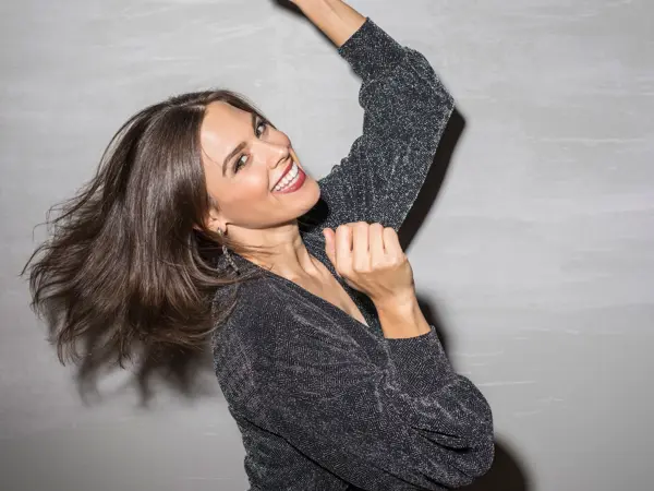 Jente i svart glitterkjole danser og smiler mot kamera