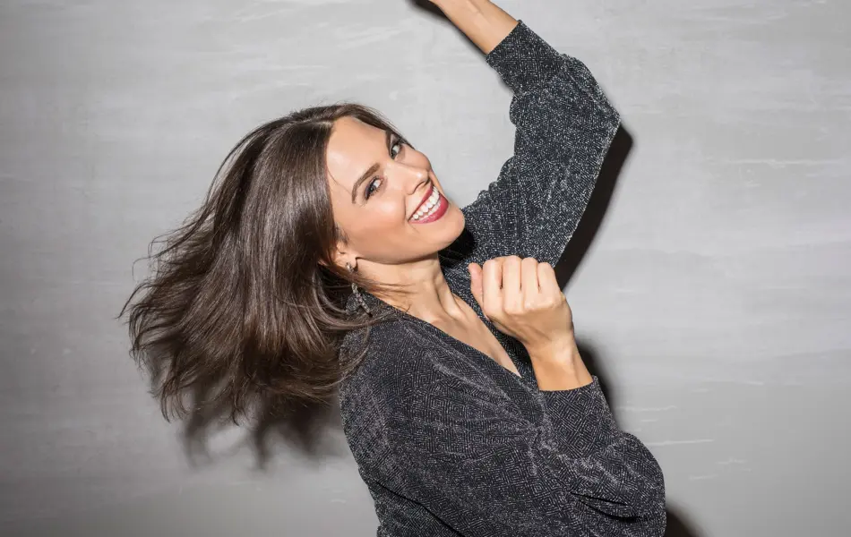 Jente i svart glitterkjole danser og smiler mot kamera