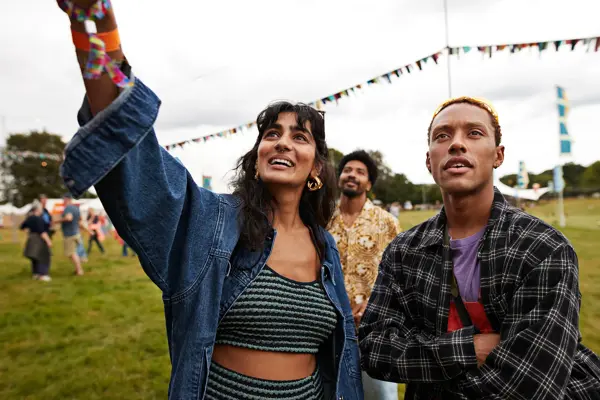 Dame med stripete topp og olajakke står sammen med mann i rutete skjorte med festival i bakgrunnen