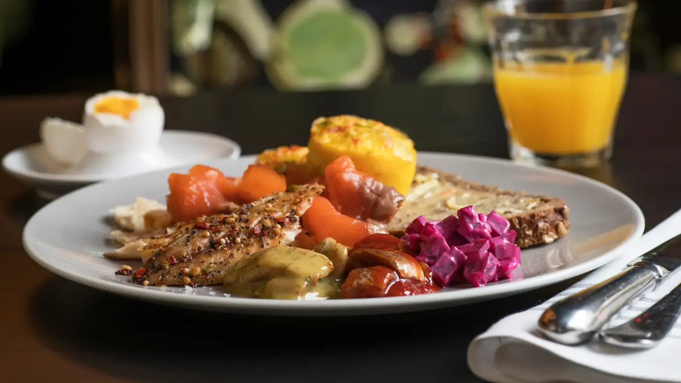 Frokosttallerken med grovt brød, laks, sild, rødbetsalat, kokt egg og et glass ferskpresset appelsinjuice.