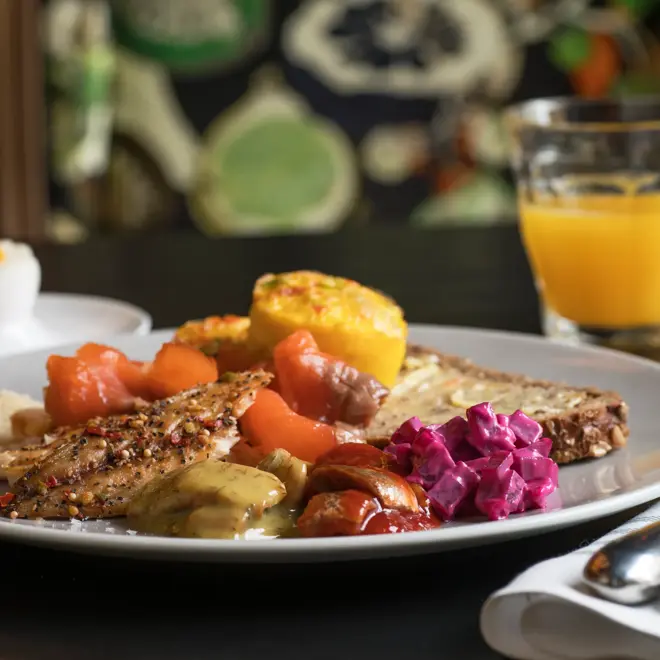 Frokosttallerken med grovt brød, laks, sild, rødbetsalat, kokt egg og et glass ferskpresset appelsinjuice.