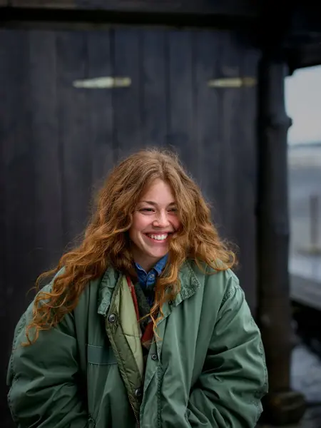 Dame i stor, grønn jakke og langt, bølgete hår smiler utendørs 