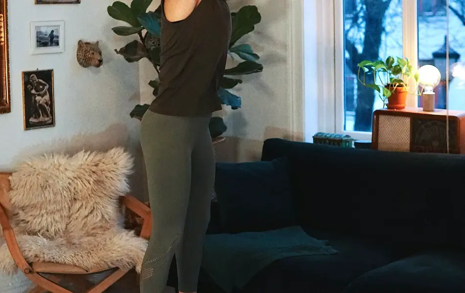 treningsekspert Anna Johansen trener på matte på gulvet, mørkegrønn sofa i bakgrunnen, lys stol med pels oppi, str grønn plante, bilder på veggen