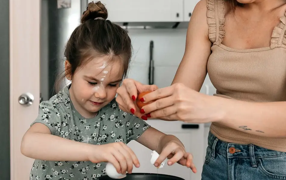 Jente baker sammen dame på kjøkkenet, diverse interiørartikler og ingredienser i uskarp forgrunn. Foto til artikkel om gavetips til farsdag.