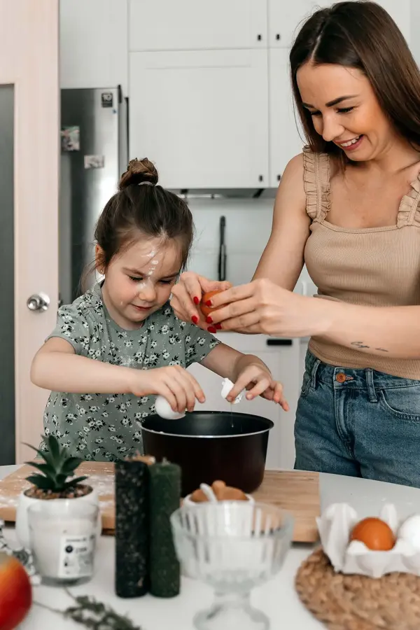 Jente baker sammen dame på kjøkkenet, diverse interiørartikler og ingredienser i uskarp forgrunn. Foto til artikkel om gavetips til farsdag.