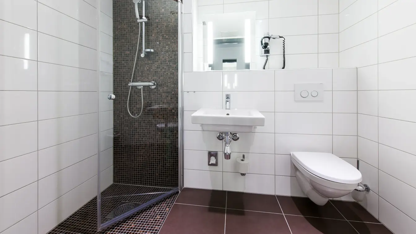 Brune gulvfliser, hvite veggfliser, toalett, vask, dusj