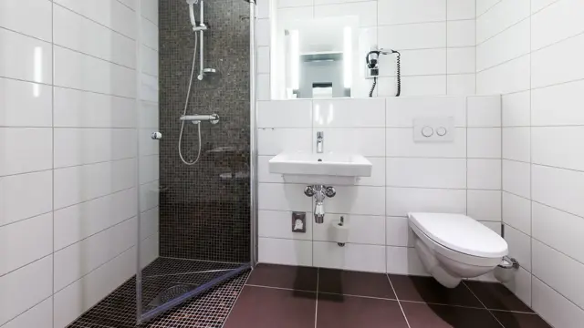 Brune gulvfliser, hvite veggfliser, toalett, vask, dusj