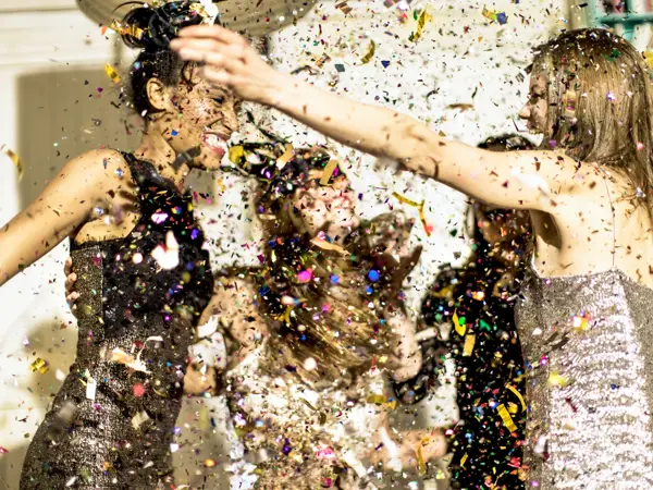 Group of young women celebrating at a party in a haze of falling glitter confetti.