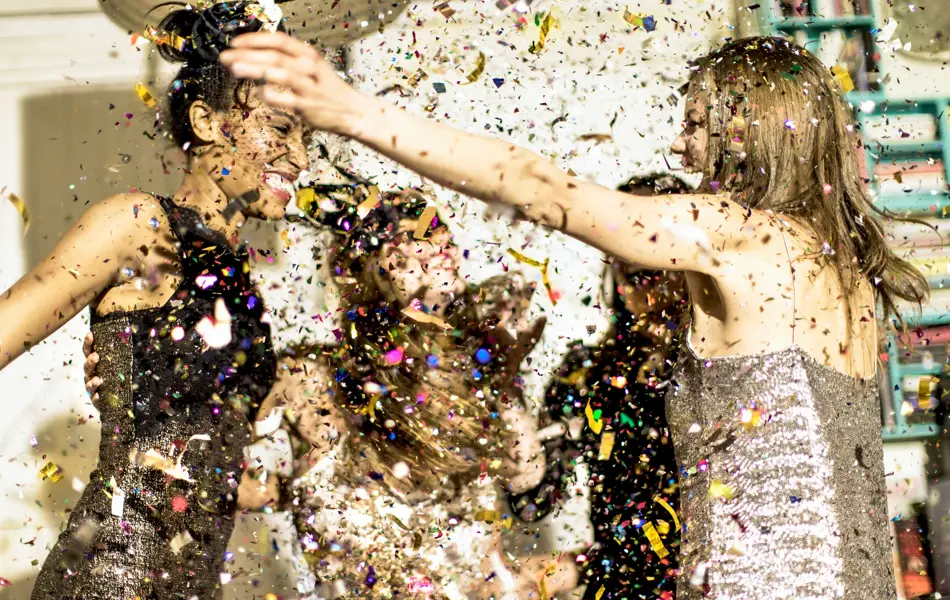 Group of young women celebrating at a party in a haze of falling glitter confetti.
