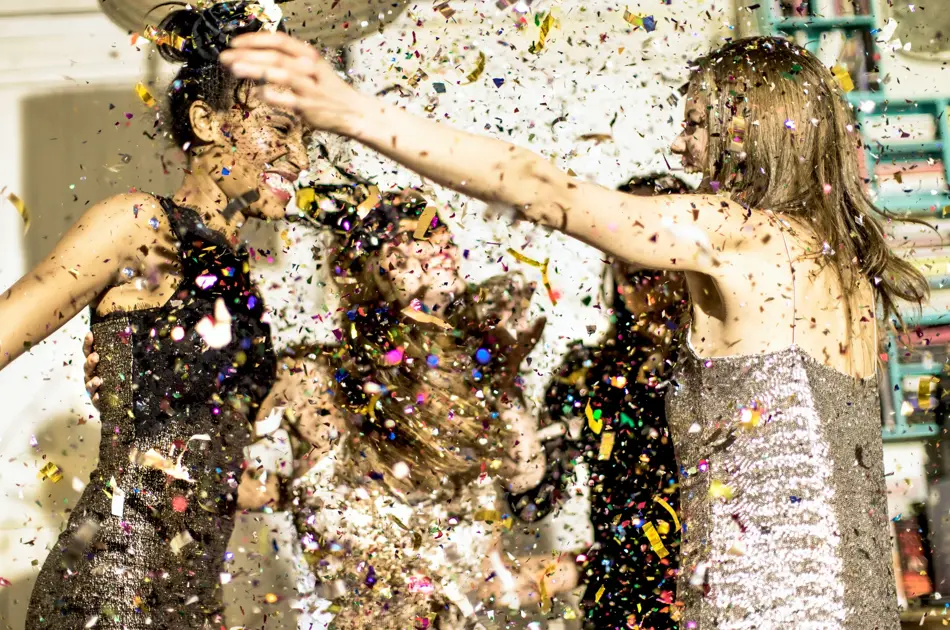 Group of young women celebrating at a party in a haze of falling glitter confetti.