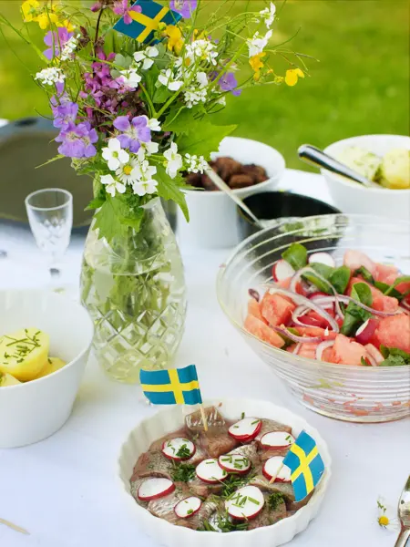 Bord med salat, sild, poteter og fargerik bukett med svenske flagg
