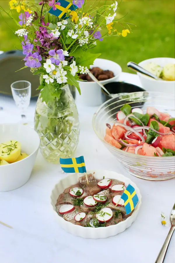 Bord med salat, sild, poteter og fargerik bukett med svenske flagg