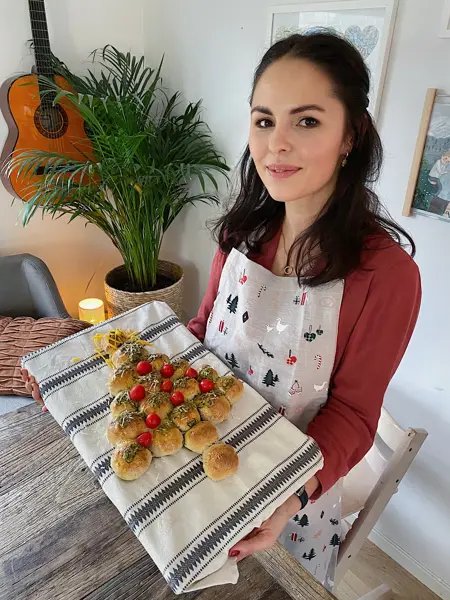 Kvinne som holder opp et bakebrett med et spiselig juletre laget av boller