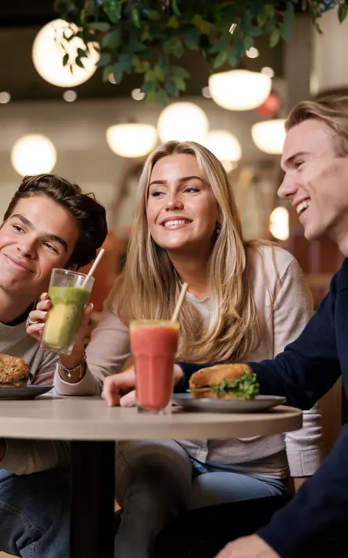 To gutter og en jente som sitter ved et bord i en kafé og tar bilder av seg selv med en mobil