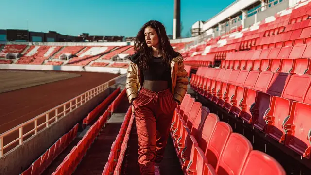 dame som går på tribunen med gull boblejakke, gjennomsiktig sort topp og røde bukser