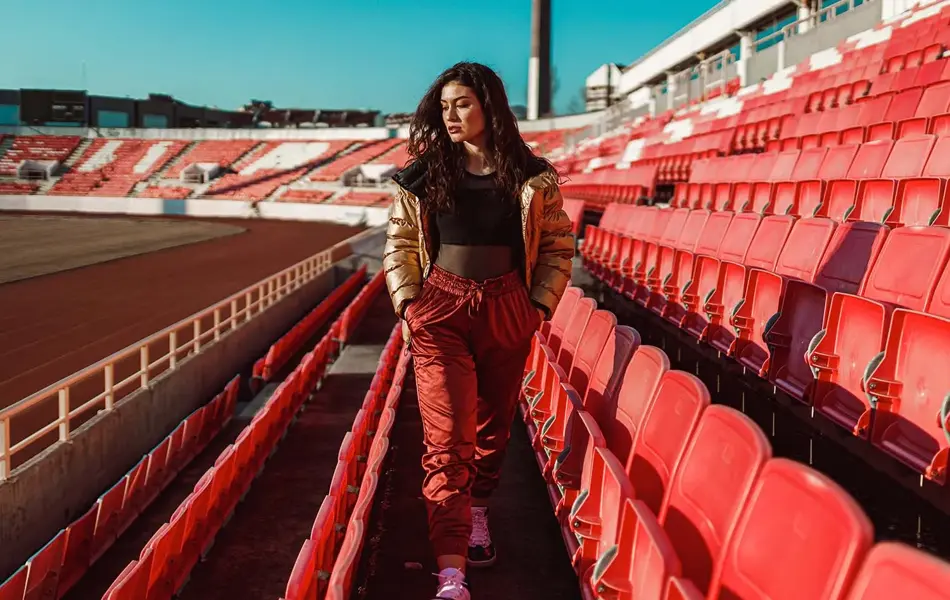 dame som går på tribunen med gull boblejakke, gjennomsiktig sort topp og røde bukser