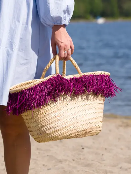 Nærbilde av hånd som holder strandveske i strå med lilla frynser.