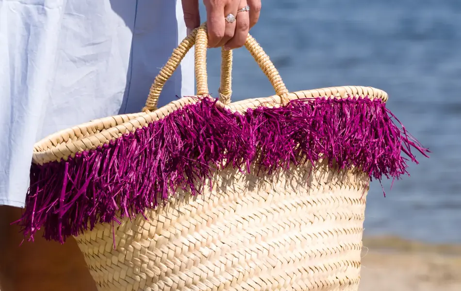 Nærbilde av hånd som holder strandveske i strå med lilla frynser.