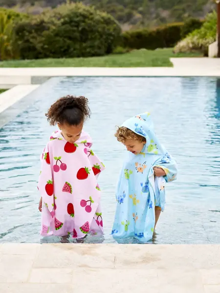 To barn med badeponcho som står ved bassengkanten