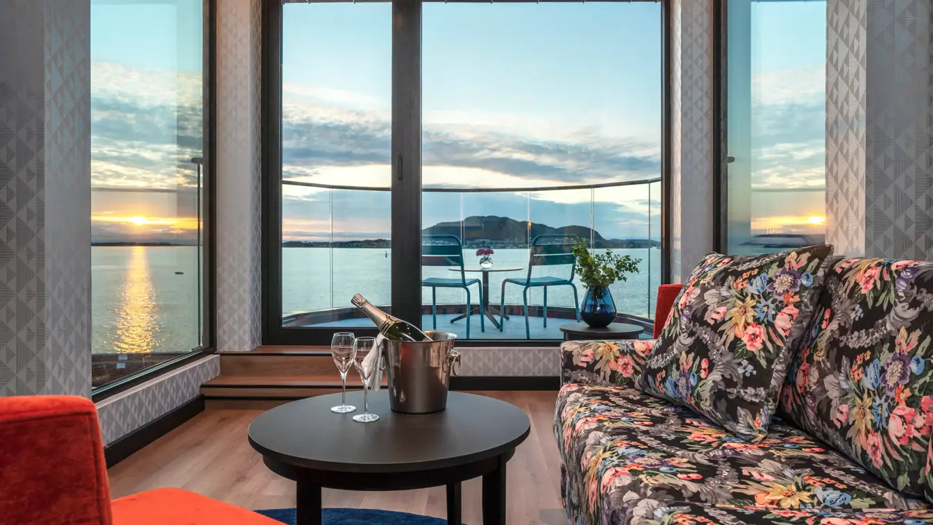 Panoramavindu med utsikt over vannet og solnedgang, rød lenestol, salongbord, sofa