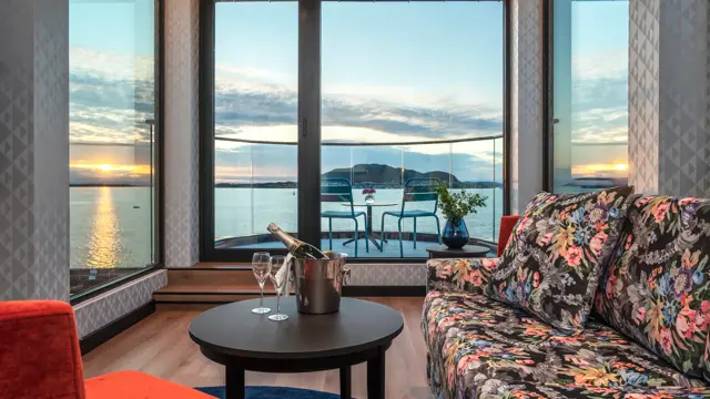 Panoramavindu med utsikt over vannet og solnedgang, rød lenestol, salongbord, sofa