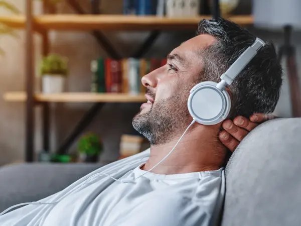 Middle aged man listening music with headphones relaxed in sofa at his home