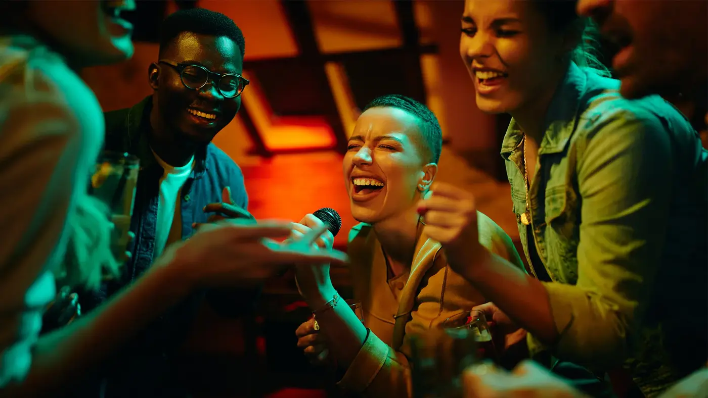 dame som synger karaoke med flere mennesker rundt henne