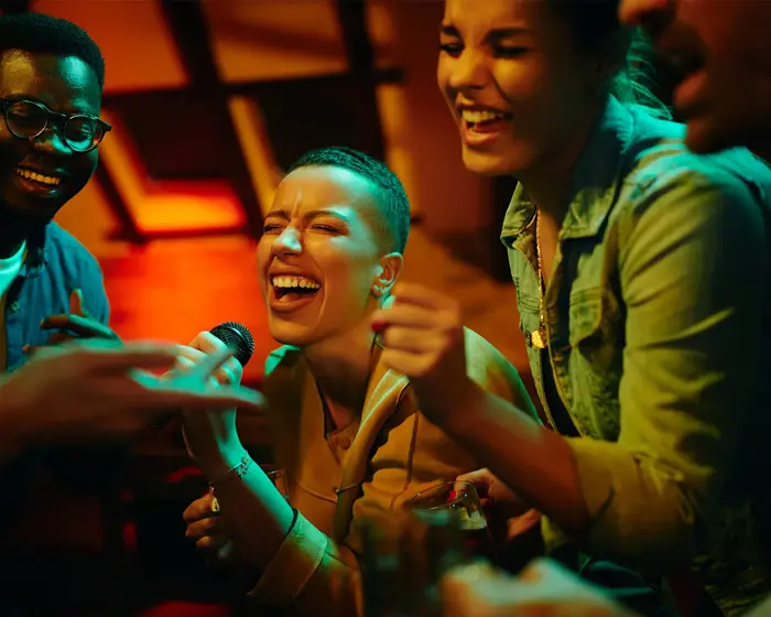 dame som synger karaoke med flere mennesker rundt henne