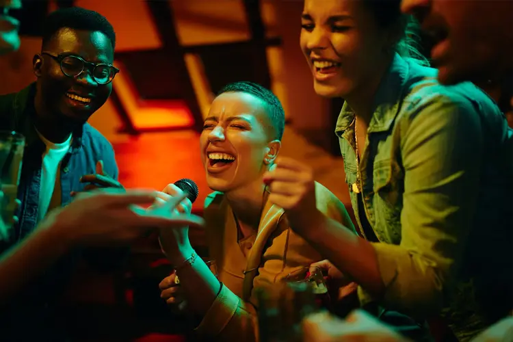 dame som synger karaoke med flere mennesker rundt henne