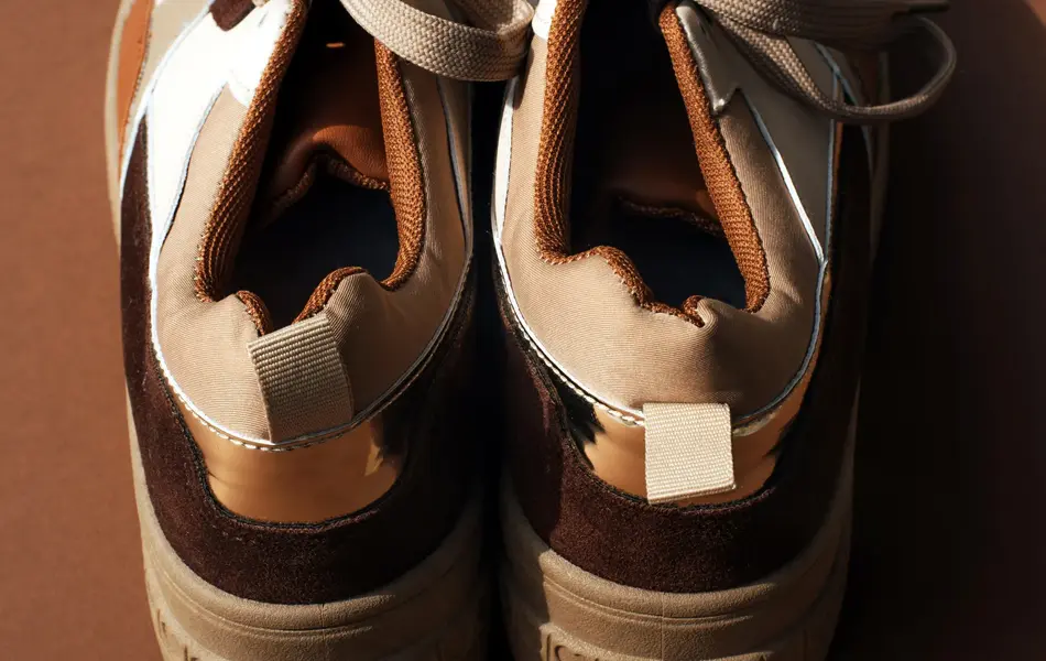 Nærbilde av sneakers med brune detaljer på brun bakgrunn sett bakfra 