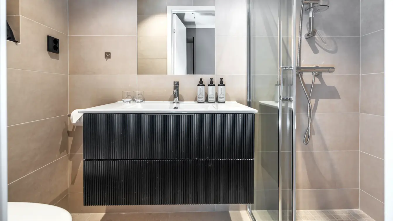 Flislagt bad med servantskap, speil, og dusj.